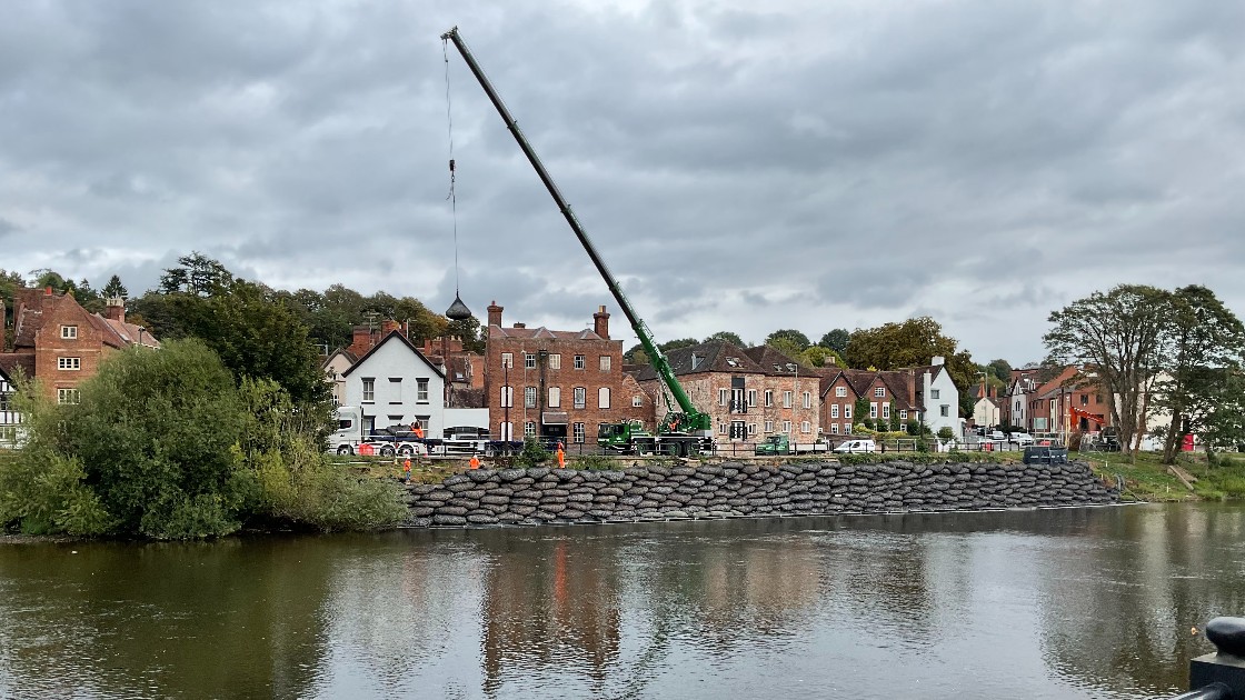 Crane placing bags of rocks on the bank of the river Severn