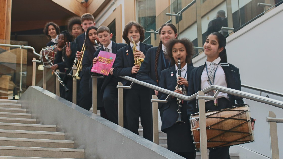 Several year 7 students holding instruments and a programme.