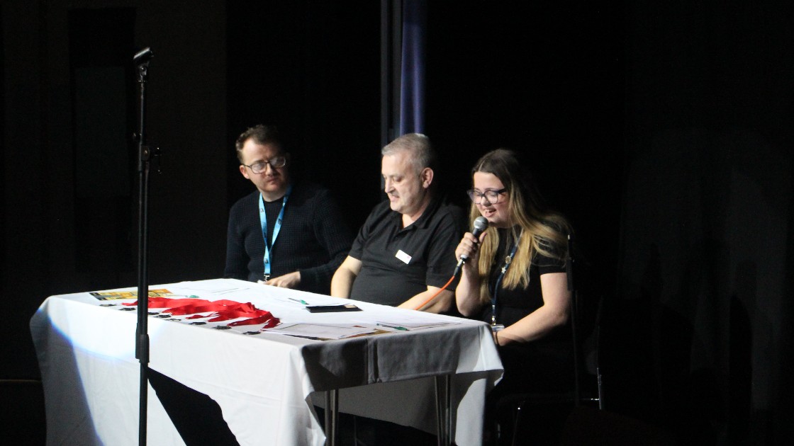 Three judges sit making notes and giving feedback.