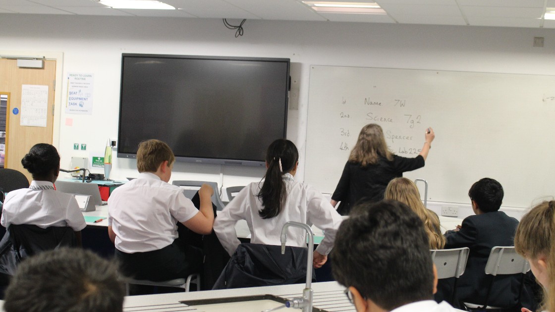 Teacher writing on whiteboard in classroom with Year 7 students seated at desks