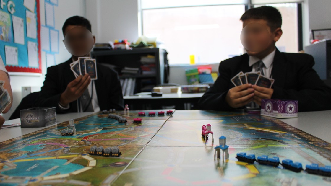 Two students playing a board game with cards and a game board