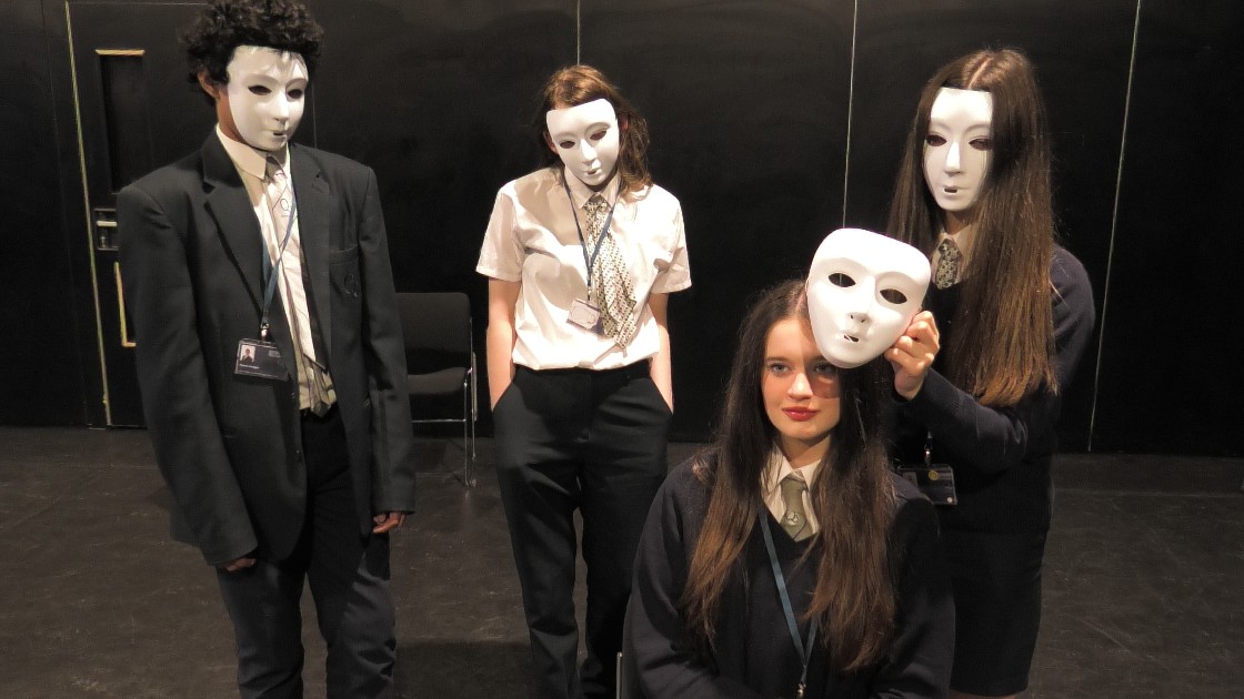 Students in school uniforms wearing white masks during a drama lesson
