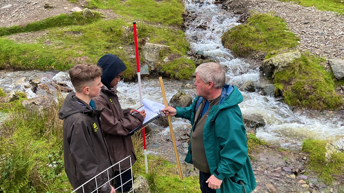 A teacher and two students conducting a field study by a stream in Carding Mill Valley