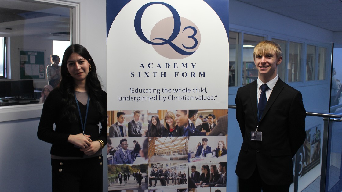 Two students standing beside a Sixth Form banner