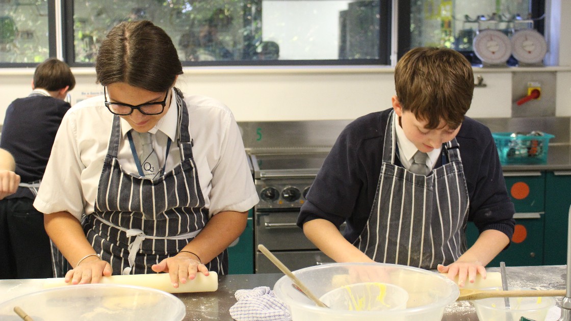 Two students in aprons rolling dough in a kitchen