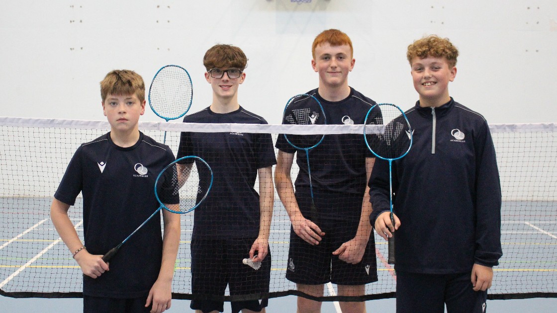 Four students holding badminton rackets in a sports hall