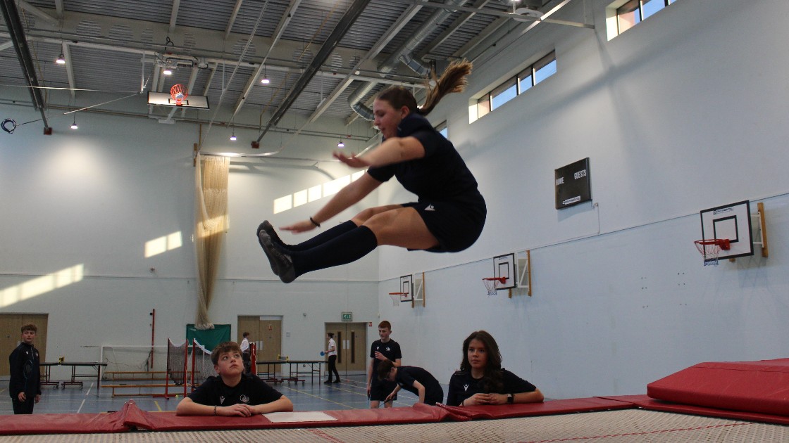 Student performing a jump on a trampoline in a gymnasium