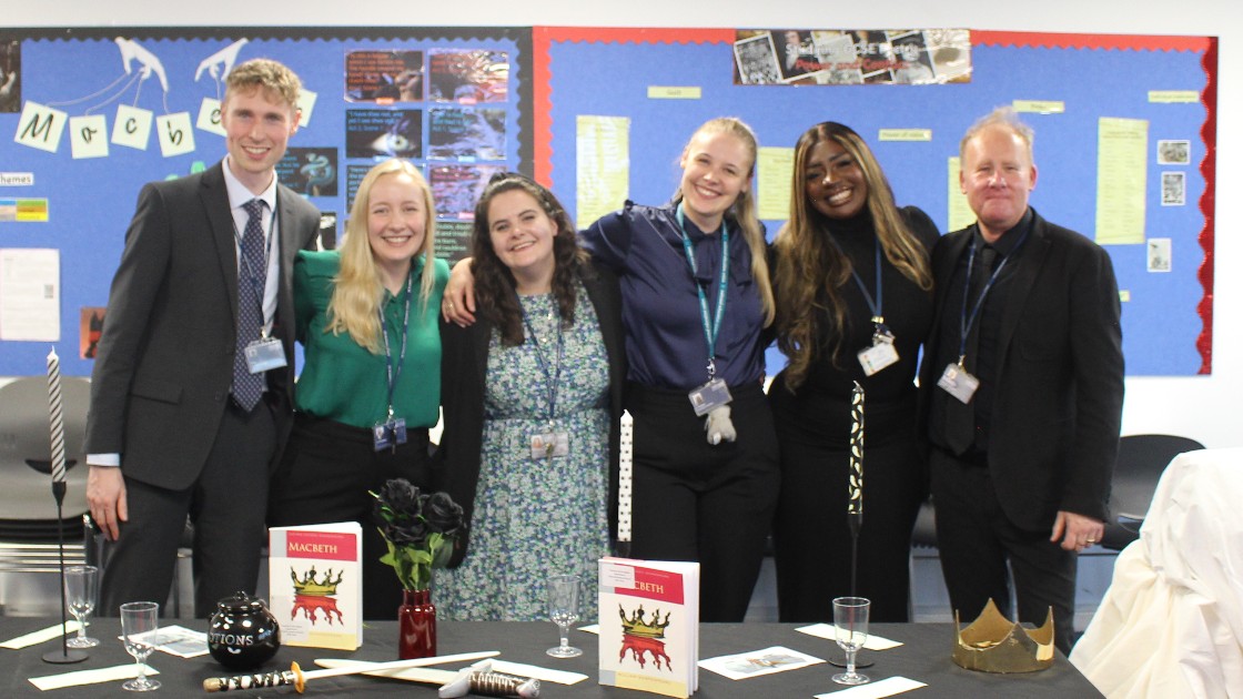 Teachers standing together in a classroom with Macbeth-themed decorations on the table
