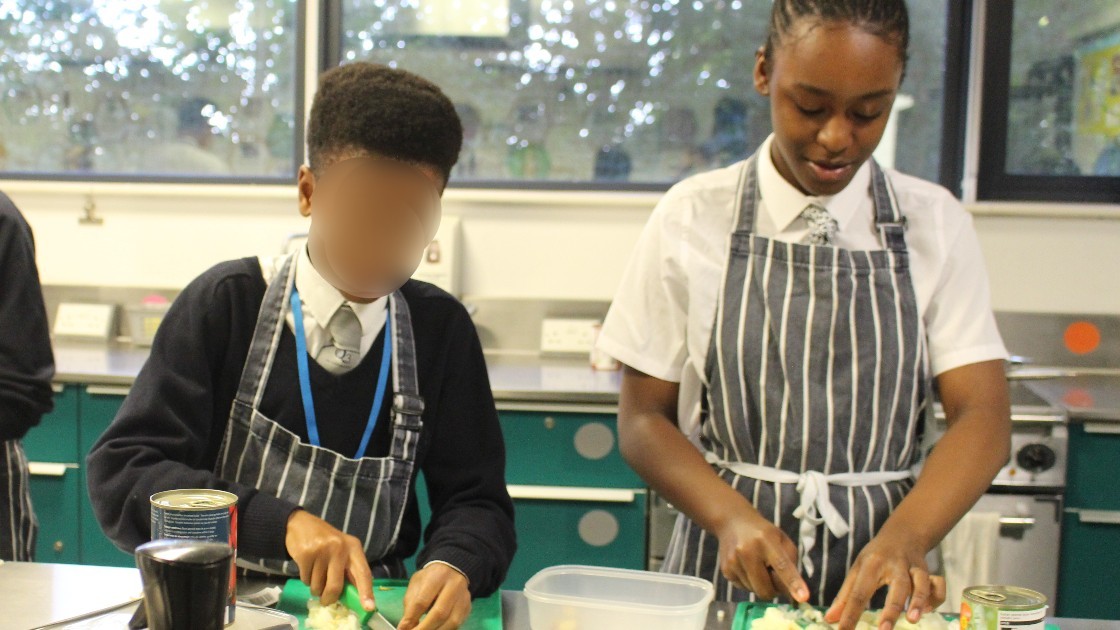 Two students in aprons chopping vegetables in a kitchen