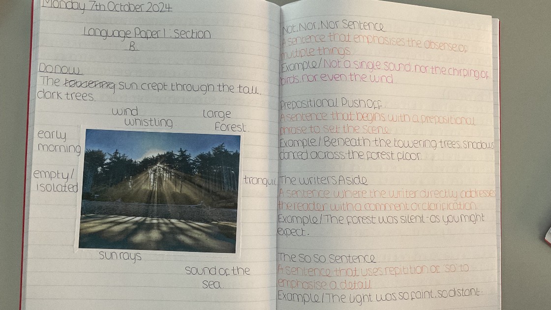 An open exercise book with handwritten notes on English language, including a photo of a forest. The notes cover topics like sentence types and prepositional phrases