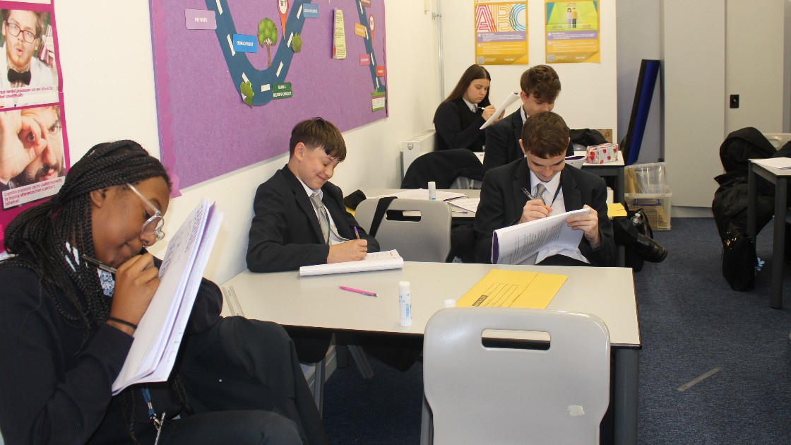 Students in a classroom writing in notebooks during a psychology lesson