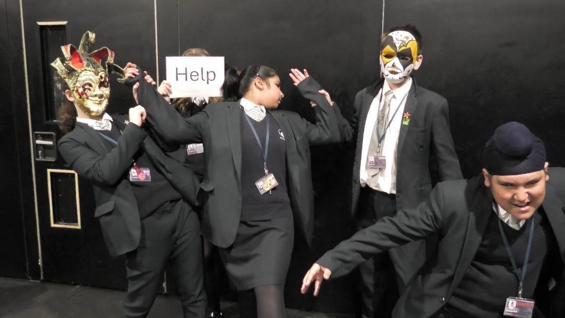 Students in masks and costumes performing a dramatic scene