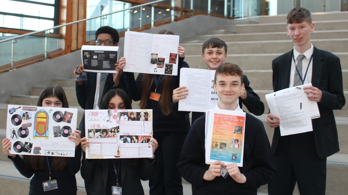 Students holding up their GCSE Music coursework in front of a staircase