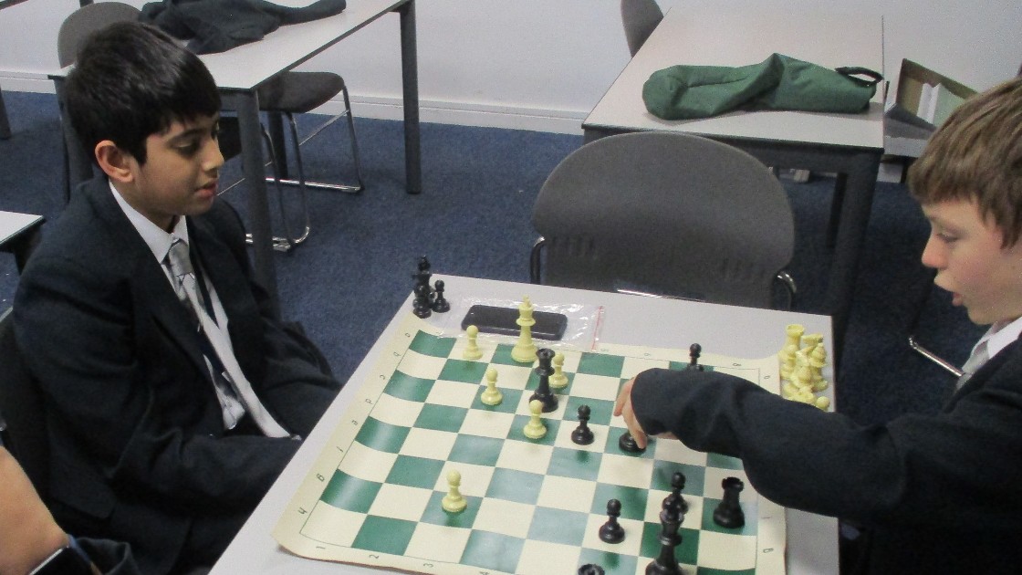 Two students playing chess at a table in a classroom