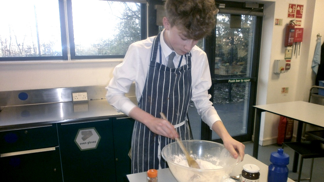 A student in an apron mixing ingredients in a bowl during a food lesson