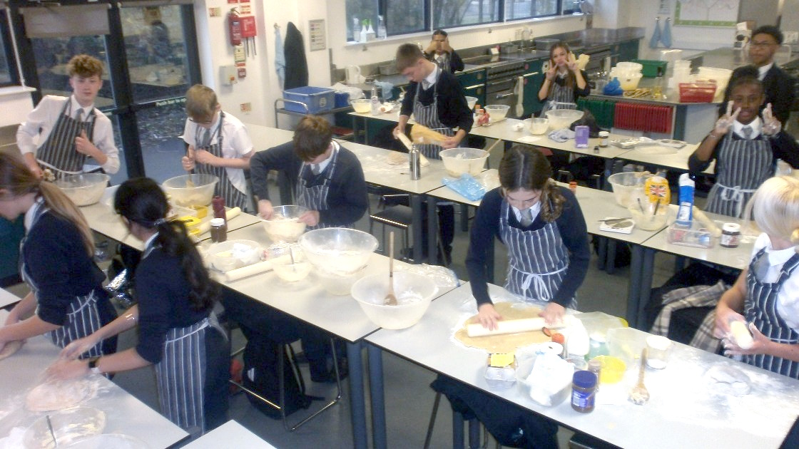 Students in aprons working on baking tasks in a classroom