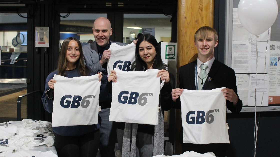 Students with the headteacher holding GB6th-branded tote bags at an event