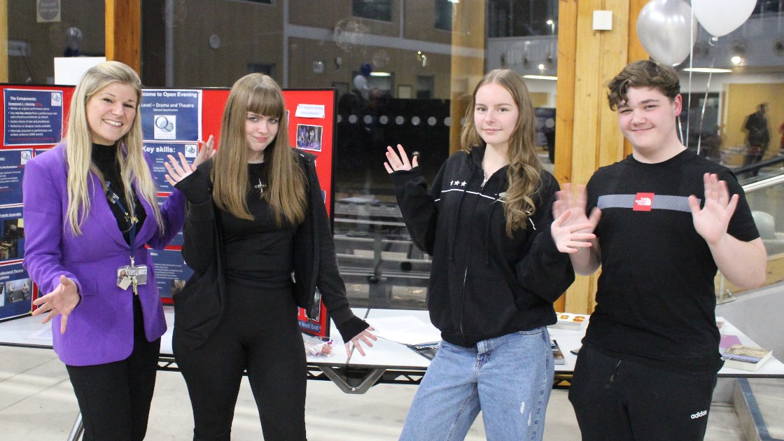 A drama teacher and three students standing near a display table