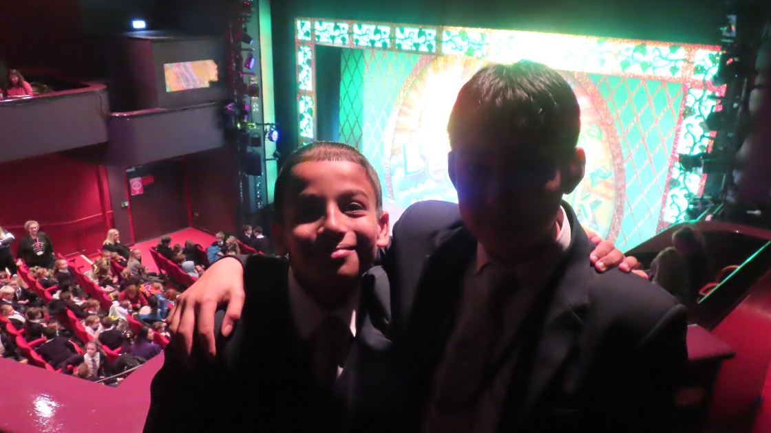Two students in school uniforms at a theatre with a colourful stage in the background