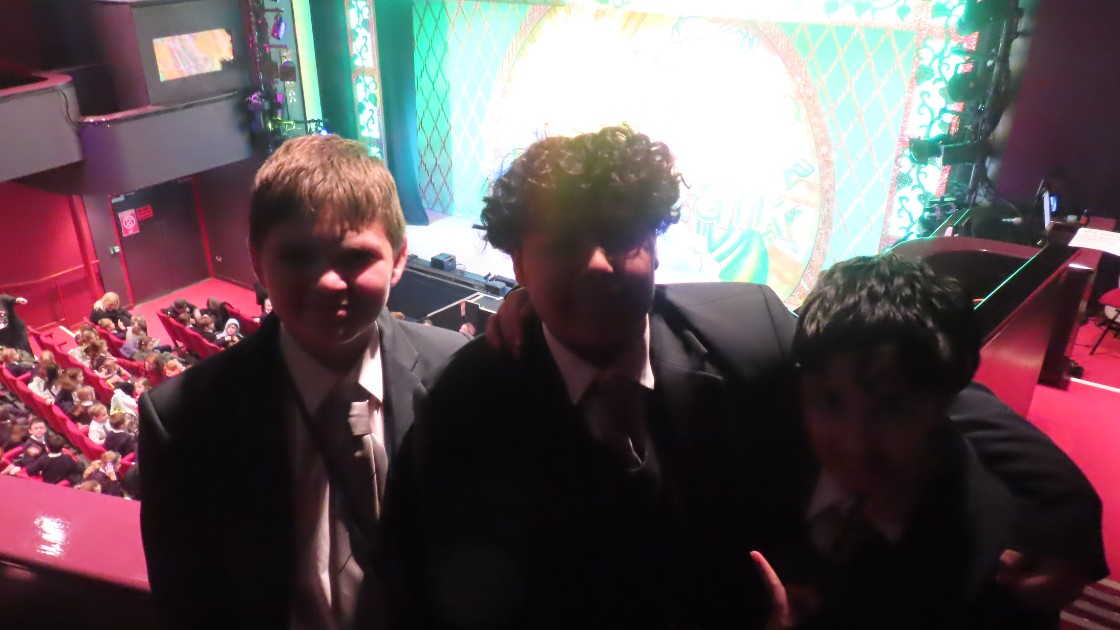 Three students in school uniforms at a theatre with a stage in the background