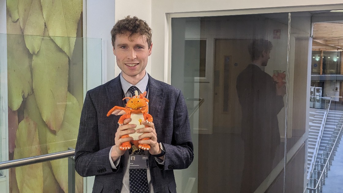 A teacher holding an orange dragon toy in a school corridor