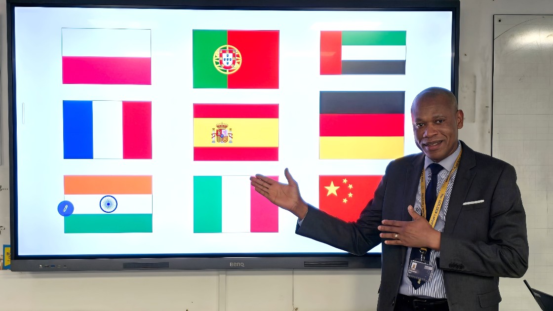 A teacher standing next to a screen displaying flags of various countries