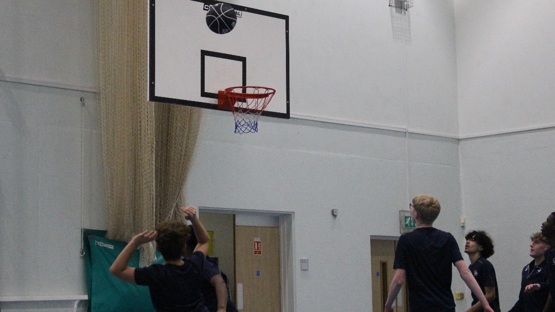 Students playing basketball in a gymnasium, with a ball near the hoop