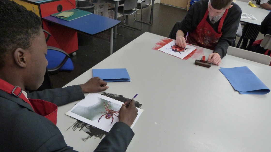 Students working on art projects at a table, creating designs with paint and paper