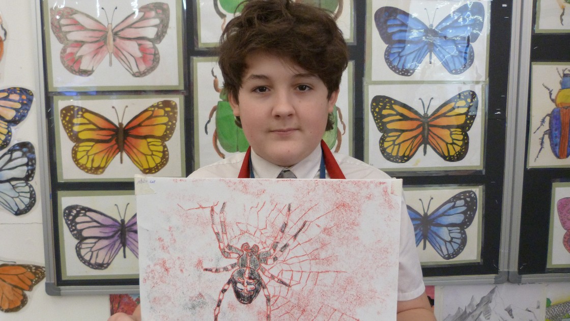 A student holding a spider-themed artwork in front of a display of butterfly illustrations