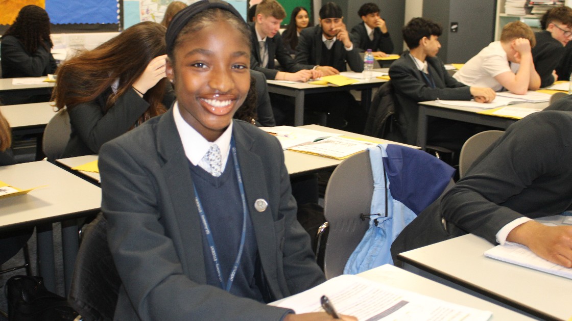 A student in a classroom smiling during a Geography lesson