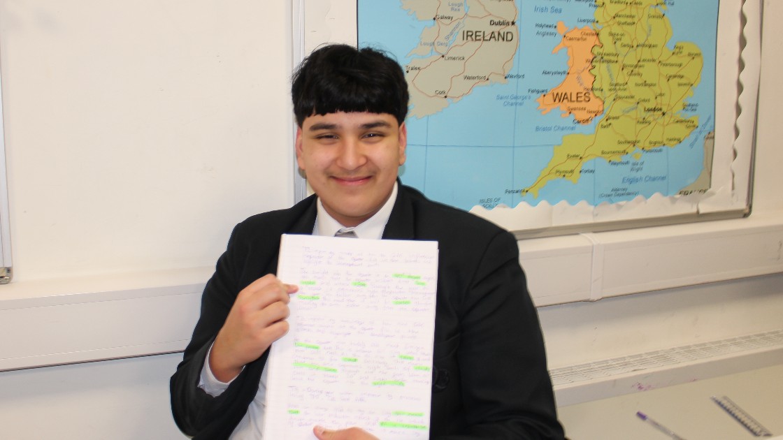 A student holding a piece of written work in a classroom with a map of the UK and Ireland on the wall