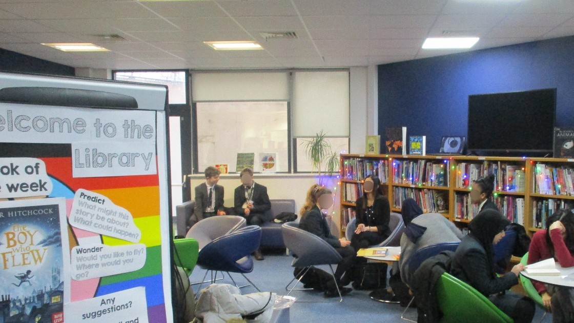Students sitting in a library with bookshelves and a display board