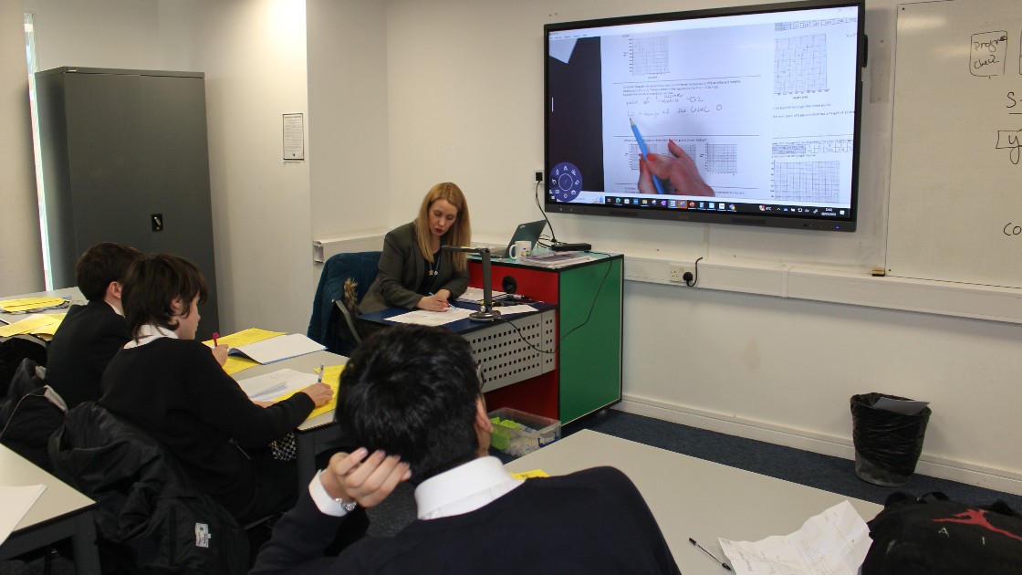 A teacher using a visualiser to demonstrate a statistics problem to students in a classroom
