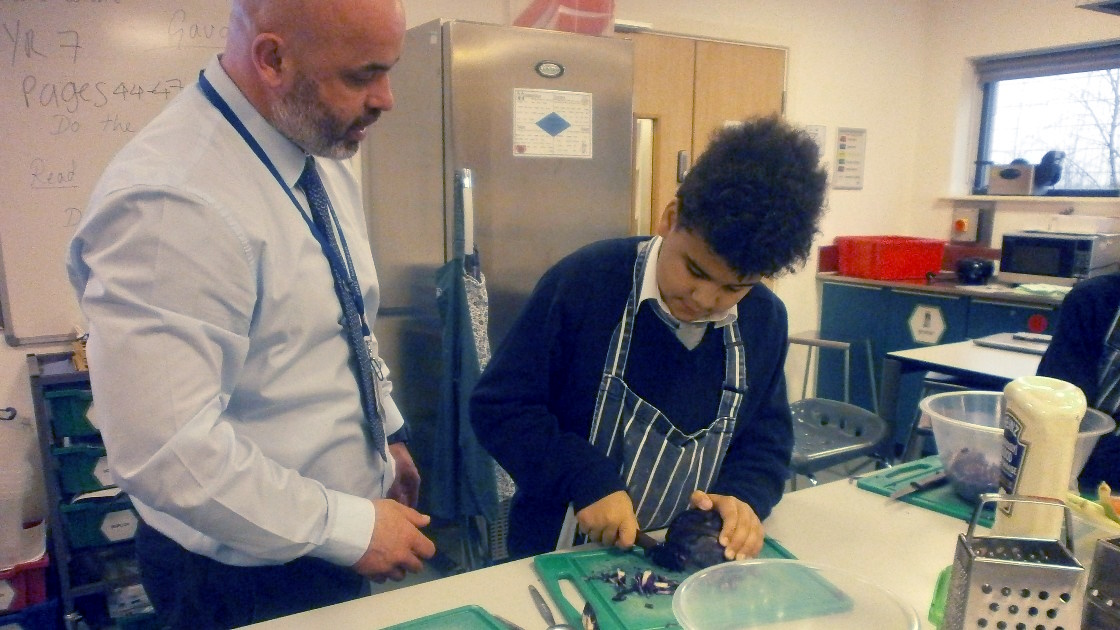 A teacher observing a student chopping vegetables in a classroom