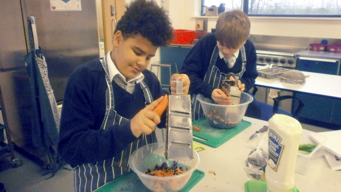 Two students grating vegetables in a food lesson