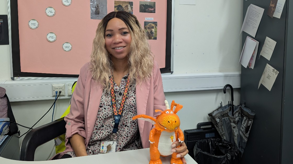 A teacher sitting at a desk holding a small orange dragon toy