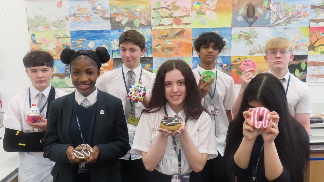 Students holding colourful clay doughnuts in an art classroom