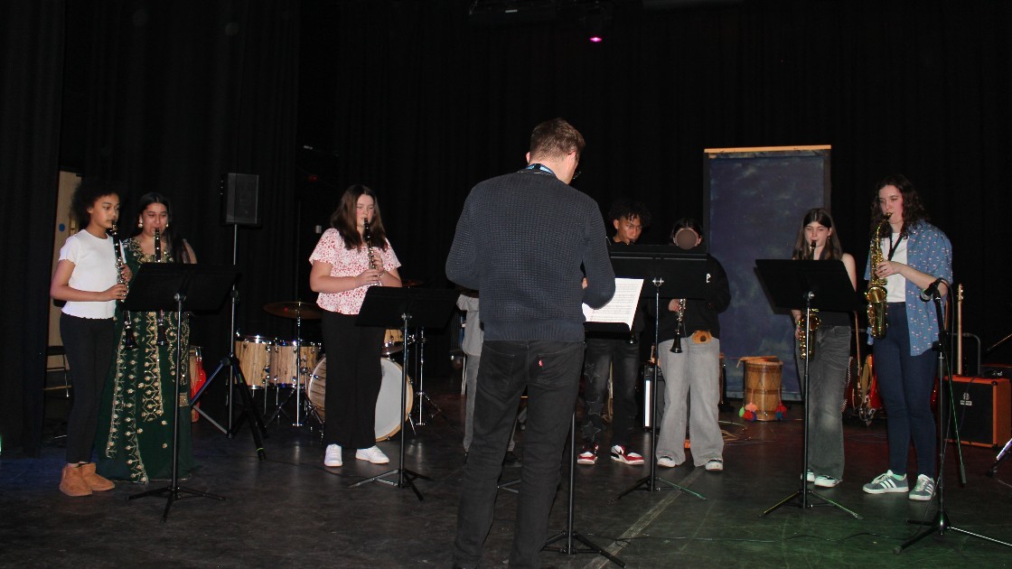 A group of students performing music on stage with a teacher conducting
