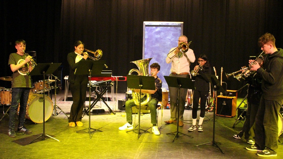 A group of students and a teacher playing brass and wind instruments on stage