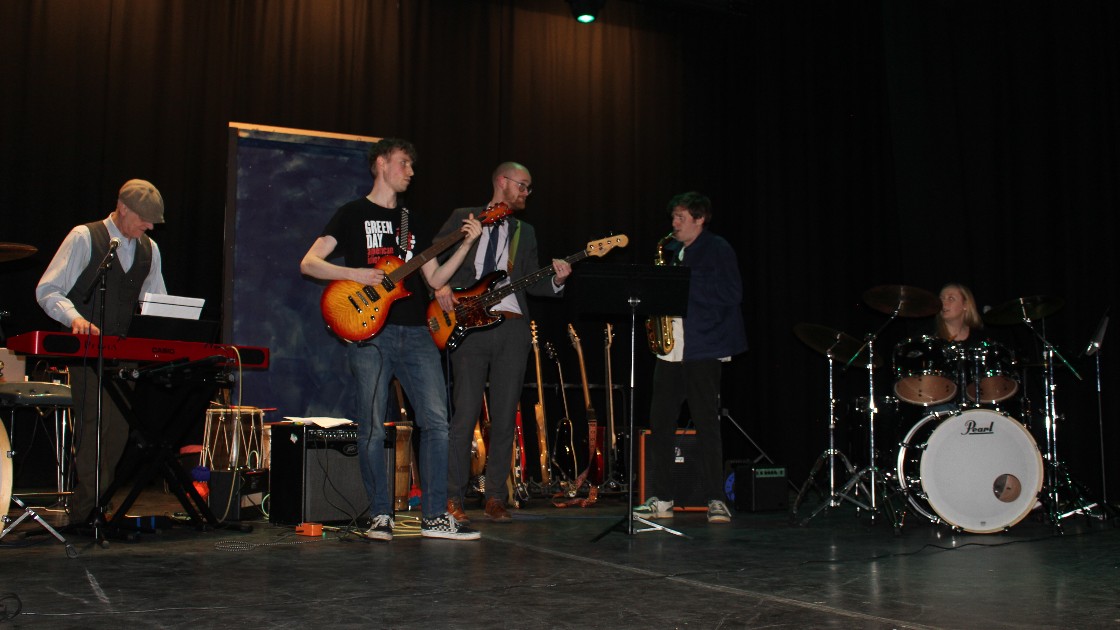 A group of students and a teacher performing on stage with musical instruments
