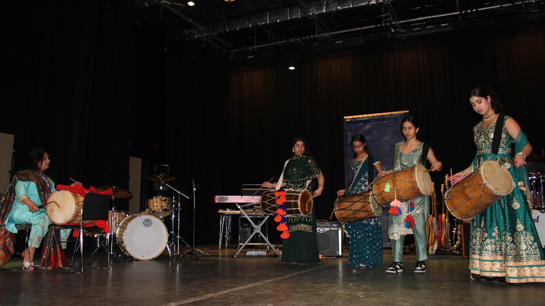 A group of students performing on stage with traditional drums and other musical instruments