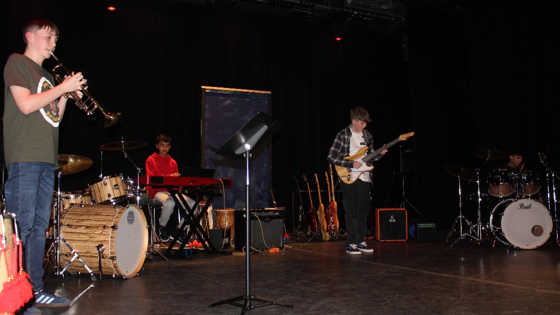 A student band performing on stage with a clarinet, keyboard, electric guitar, and drums