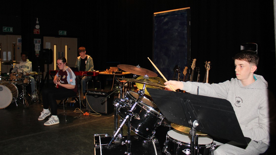 Students performing in a band with drums, guitar, and other instruments