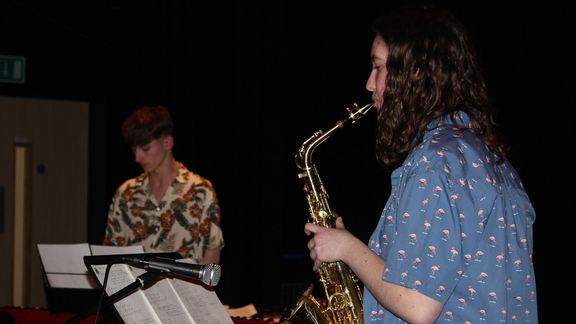 Two students performing music, one playing a saxophone and the other on a keyboard