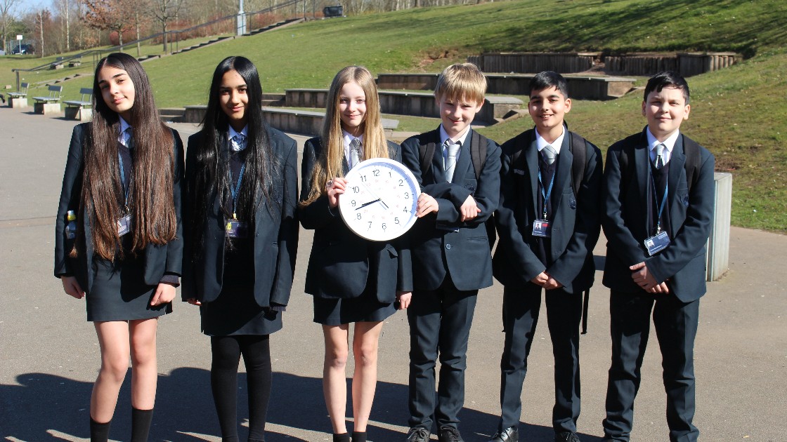 Students in school uniforms holding a large clock outdoors