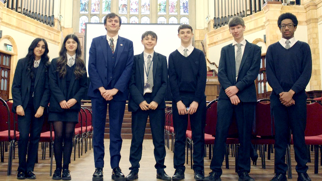 Year 10 students and a teacher standing in a hall with stained glass windows
