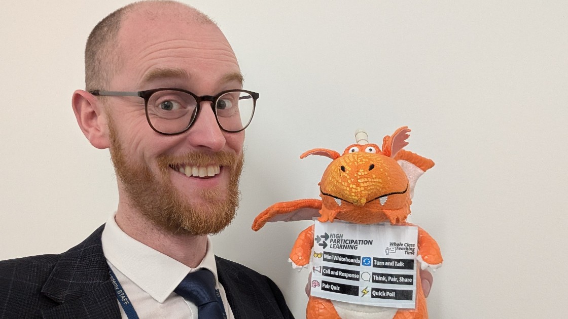 A teacher holding an orange dragon plush toy with educational labels