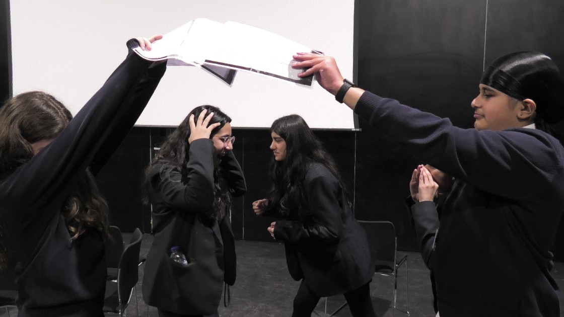 Students in a drama lesson acting out a scene with expressive gestures