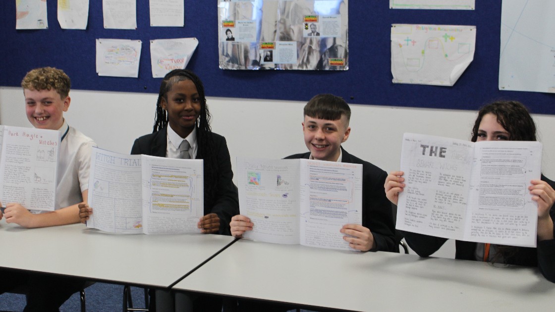 Four students sitting at a table holding up their written and illustrated projects