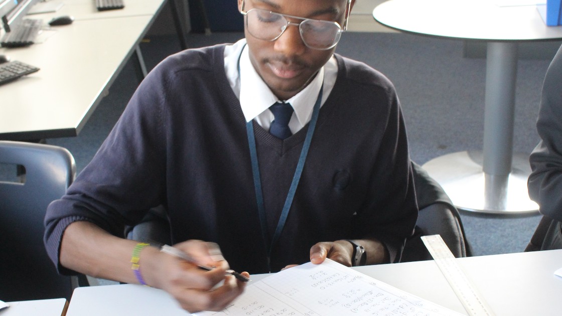 A student in a classroom writing in a notebook during a maths lesson